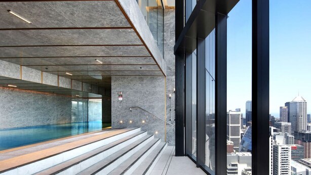 Un bâtiment moderne doté d’une piscine à débordement en verre, d’un escalier et offrant une vue sur la ville.