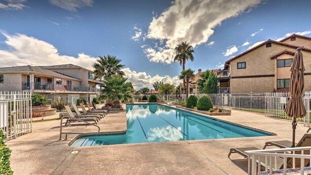 A swimming pool with lounge chairs, a white fence, and houses in the background.