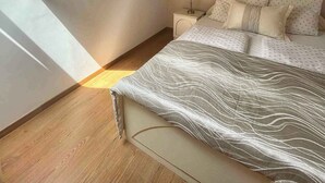 Ein Schlafzimmer mit schrägem Dach, einem Bett mit gemusterten Betttextilien, einem Nachttisch mit Lampe und einem Gemälde an der Wand.