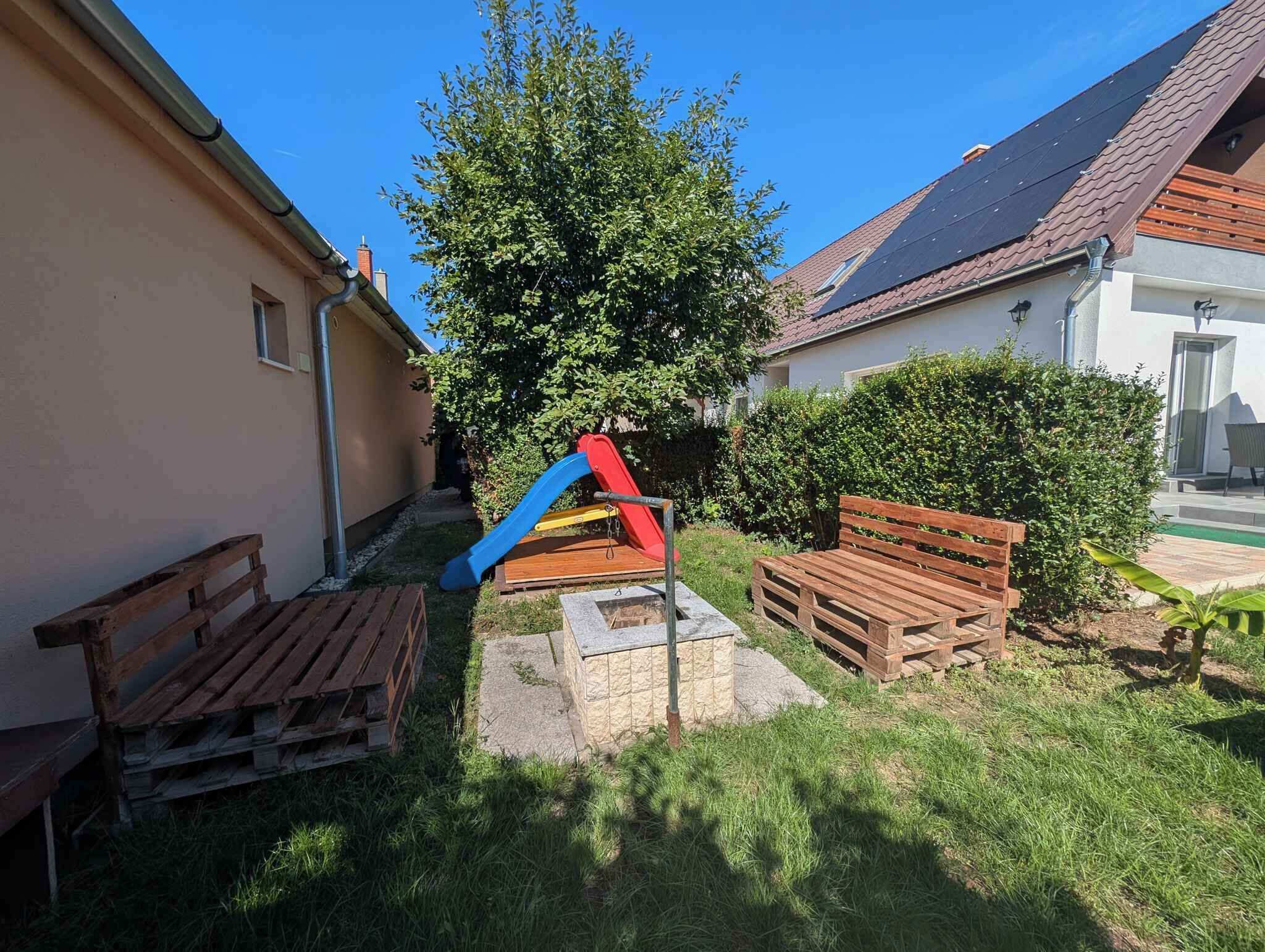 A residential outdoor area with a play structure, wooden benches, and a well-maintained lawn.