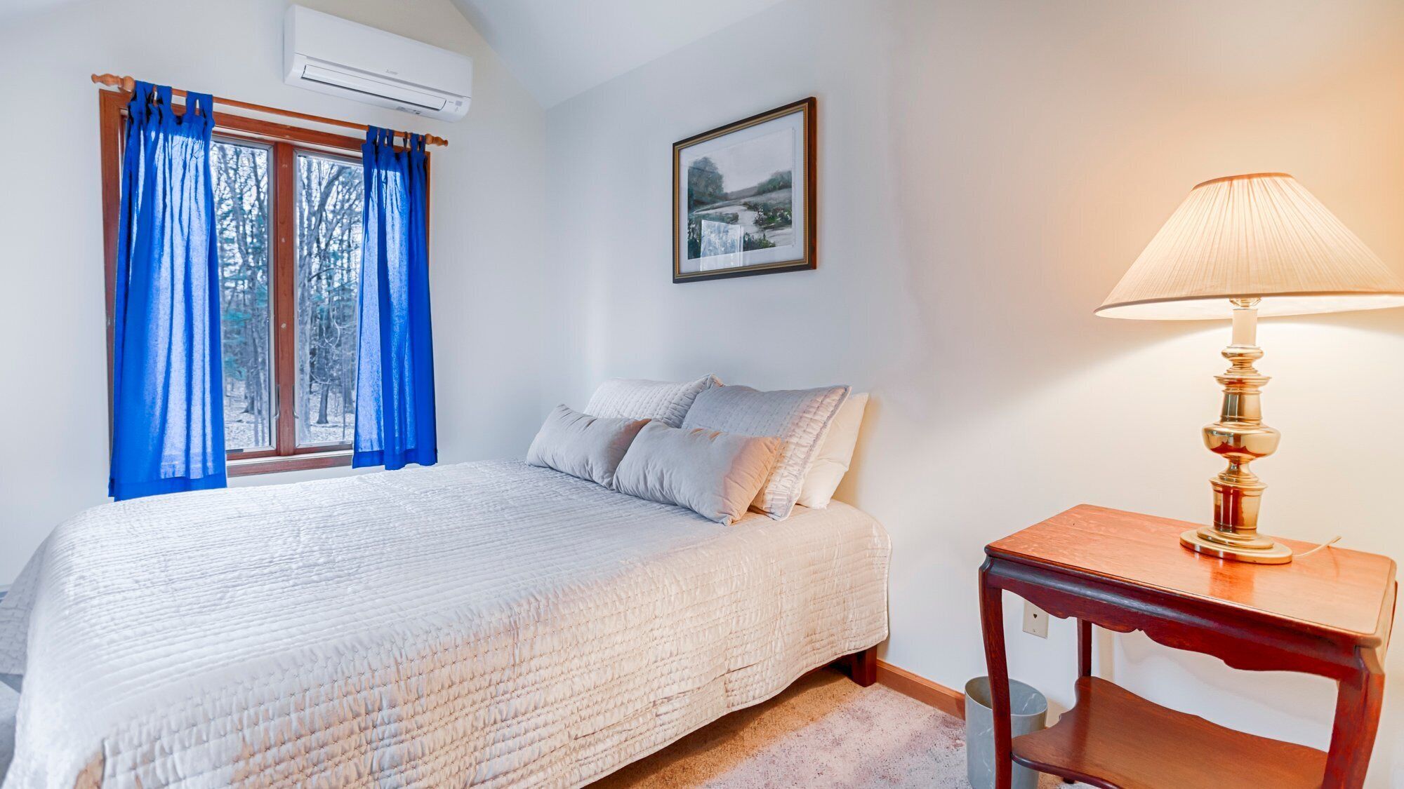 Una camera da letto con un letto, un comodino con una lampada, una finestra con tende e un quadro appeso al muro.