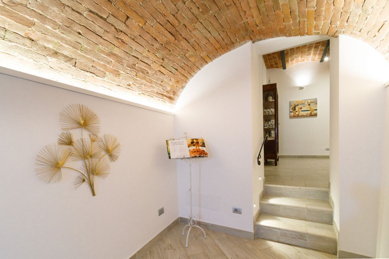 A hallway with a brick ceiling, a standing display stand, a staircase, and a framed picture on the wall.