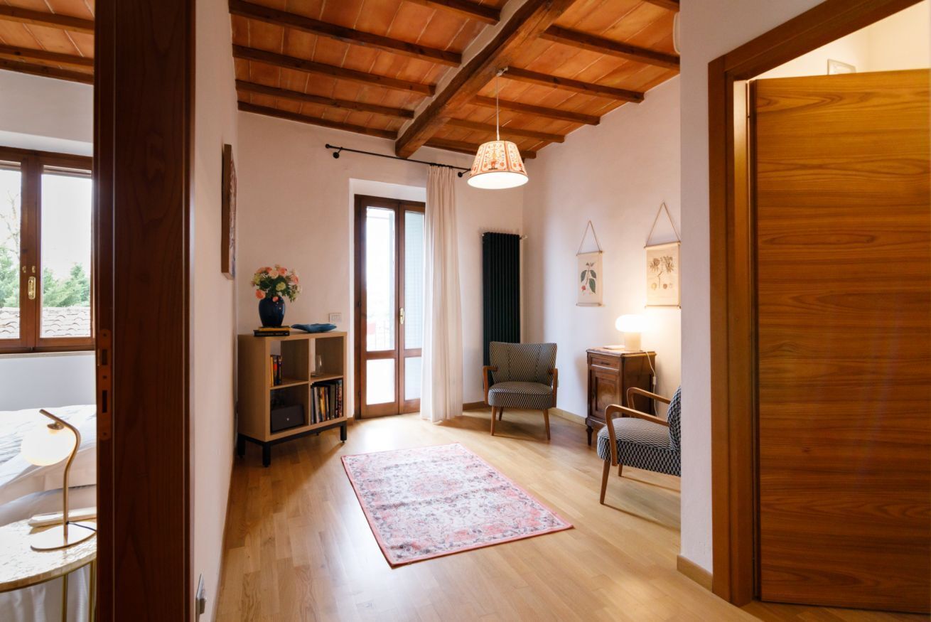A room with wooden flooring, a chair, a table, a bookshelf, and a door.