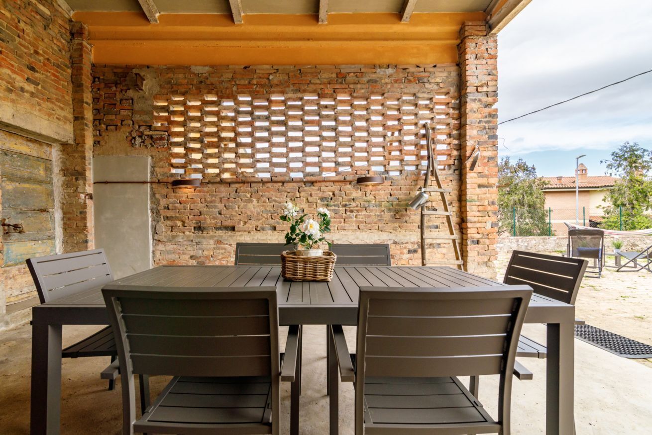 Een terras buiten, met een bakstenen muur, een houten tafel en stoelen.