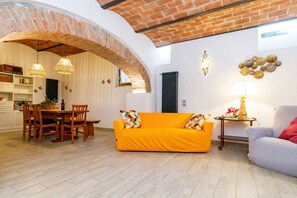 A living room with a brick archway, a dining area with wooden furniture, and a sofa with patterned cushions.