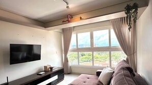 A modern living room with a flat-screen TV, a dark brown sofa, a wooden entertainment unit, and a large window with curtains. - Davisis Luxo Dunas do Jalapão (Palmas)