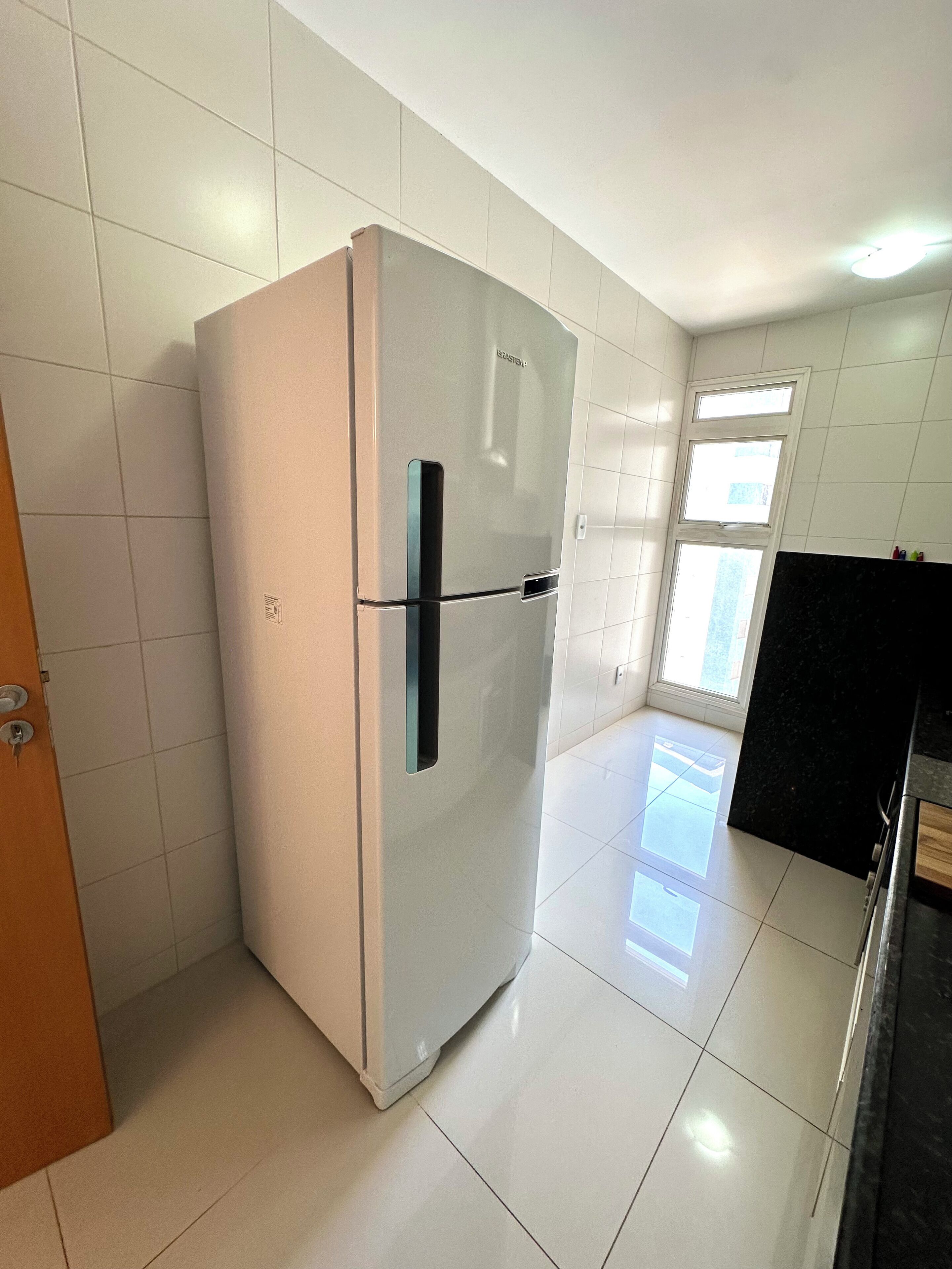Eine Küche mit weißen Fliesen, einem Edelstahl-Kühlschrank und einer schwarzen Arbeitsplatte.