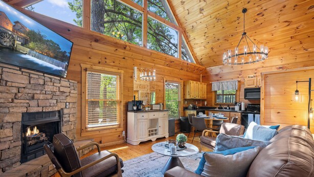 A cozy cabin interior with a stone fireplace, leather seating, a dining area, and a kitchen. - Romantic Retreat!!! Newly refreshed cabin with hot tub~New listing rates! (Sevierville)