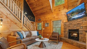 A cozy log cabin interior with a fireplace, a sofa, a coffee table, and a TV mounted on the wall. - Romantic Retreat!!! Newly refreshed cabin with hot tub~New listing rates! (Sevierville)