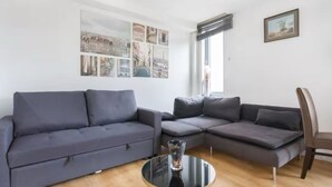 A modern living room with a grey sectional sofa, a glass coffee table, and a cityscape collage on the wall.