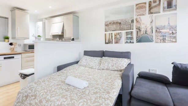 A modern bedroom with a bed, a sofa, and a small desk. There are wall-mounted cabinets and a large window.