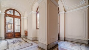 Un pasillo con suelo de mosaico, puertas de madera y paredes blancas con molduras decorativas.
