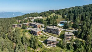 A high-rise hotel with multiple floors, surrounded by dense forest and a view of distant mountains. - Nice Apt for 4 pers near the slopes (Chamrousse)