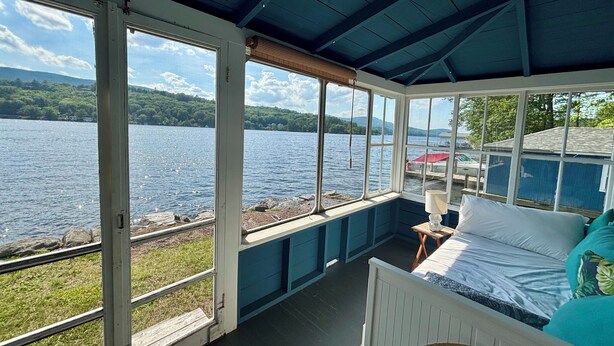 A room with a bed, a small table, and a window overlooking a lake.