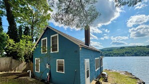 A blue house with a chimney, a wooden deck, and a view of a lake.