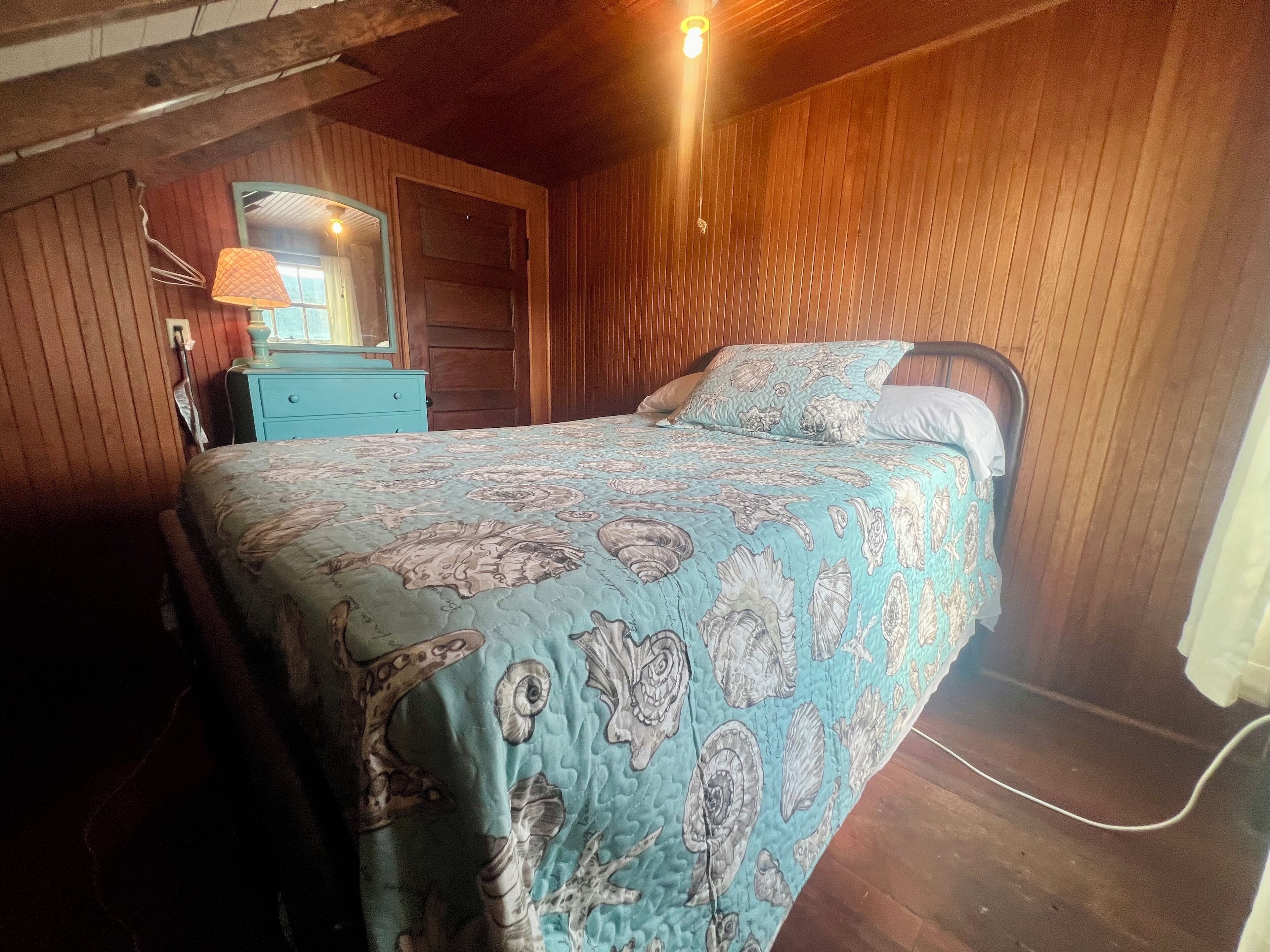 A bedroom with a bed, a dresser, a mirror, and wooden walls.