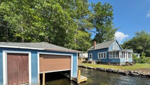 A dock extending into a calm river, with a blue house featuring a porch and a garage.