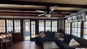 A cozy living room with a dark-colored sofa, a wooden coffee table, and a ceiling fan. Large windows provide a view of the outdoors.