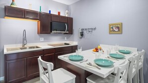 Una cocina moderna con armarios de madera oscura, una encimera blanca y un comedor con sillas blancas y platos verde azulado.