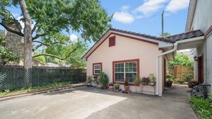 Una casa de un solo piso con techo rojo y paredes color beige, un porche con plantas en macetas y un camino de entrada que lleva al garaje.