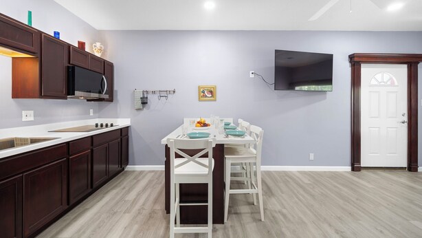 Una cocina con armarios de madera oscura, encimera blanca y comedor con sillas y mesa blancos.