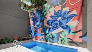 A swimming pool with a colorful mural on the adjacent wall, a wooden deck, and a metal pool ladder. - Hestia at Thames 2200 (Buenos Aires)