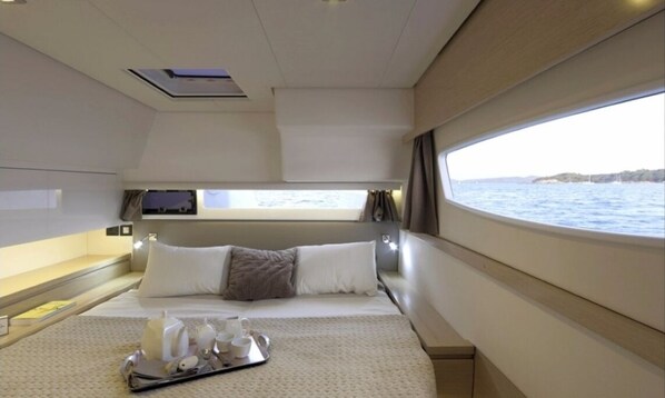 Un dormitorio moderno y luminoso con cama, almohadas, un atril con artículos de aseo y una ventana con vista al mar.