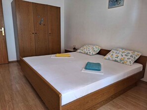 A single bed with a wooden frame, white bedding, and two pillows with floral patterns. - Holiday apartment with air conditioning, balcony and Wi-Fi internet (Punat)