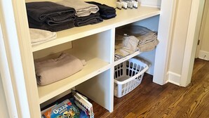 Un placard de rangement avec des étagères où sont pliées des serviettes, ainsi qu’un panier et une boîte de magazines.