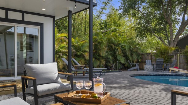 Un patio exterior moderno con piscina, sillones de descanso y zona de comedor con una bandeja de bebidas.