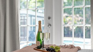 Una botella de champán, dos copas y un racimo de uvas sobre una bandeja junto a una ventana con vista a una piscina.