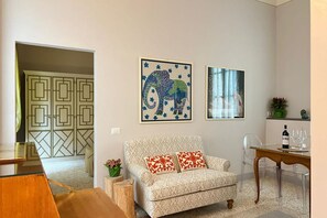 A living room with a patterned sofa, a dining table with chairs, and two framed artworks on the wall.
