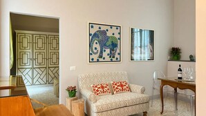Una sala de estar con un sofá estampado, una mesa de comedor con sillas y dos cuadros en la pared.