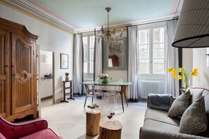 Un salon spacieux comprenant un coin repas, un lustre et un canapé agrémenté de coussins à motifs.
