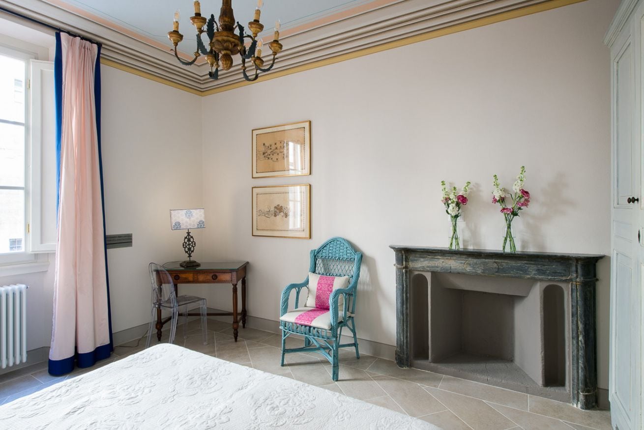 Un dormitorio con una cama, una silla, una chimenea y dos cuadros en la pared.