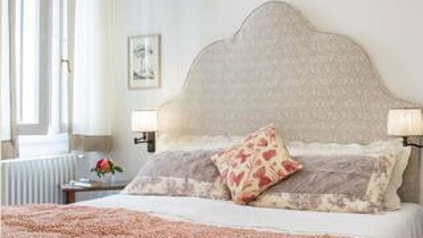 A bedroom with a large bed, two bedside lamps, a radiator, and a framed picture on the wall.