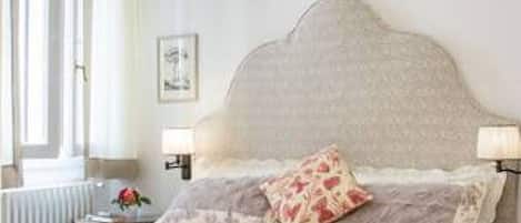 A bedroom with a large bed, two bedside lamps, a radiator, and a framed picture on the wall.