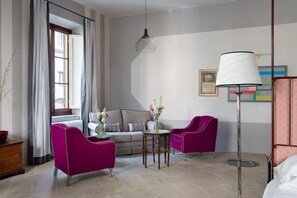 Ein Hotelzimmer mit einer Couch, zwei Sesseln, einem kleinen Tisch, einer Lampe und einem Fenster mit Vorhängen.