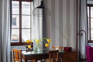 A dining area with a glass table, wooden chairs, a vase with yellow flowers, and a red bowl with a plant.