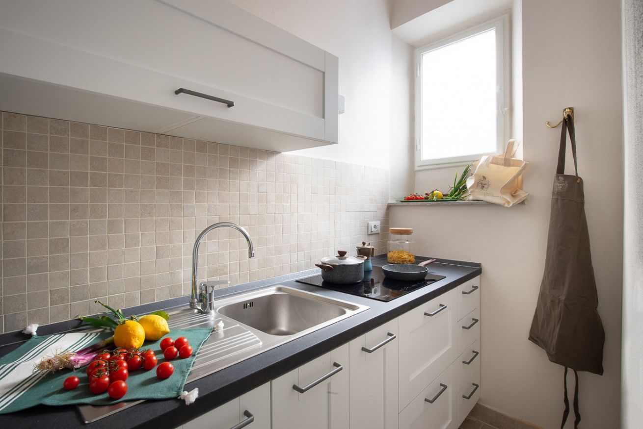 Une cuisine moderne dotée d’un évier à deux bacs, de meubles blancs, d’une fenêtre et d’un tablier suspendu.