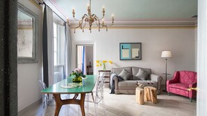 Un espace repas comprenant une table et des chaises en verre, un lustre, un canapé, un fauteuil rouge et une lampe sur pied.