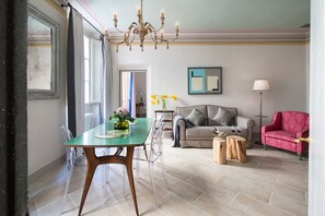 Un espace repas comprenant une table et des chaises en verre, un lustre, un canapé, un fauteuil rouge et une lampe sur pied.