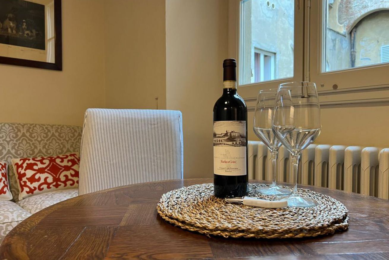 A bottle of wine on a round table with a woven placemat, accompanied by two wine glasses.