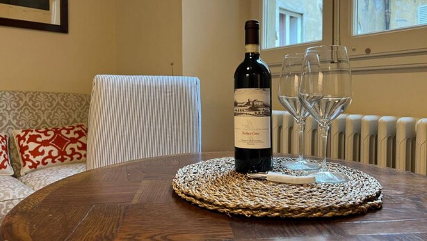 Une bouteille de vin est posée sur une table ronde recouverte d’un set de table en fibres tressées, accompagnée de deux verres à vin.