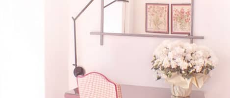 Un escritorio con un florero, una silla a cuadros y una estantería con ilustraciones botánicas enmarcadas.