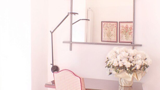 Un escritorio con un florero, una silla a cuadros y una estantería con ilustraciones botánicas enmarcadas.