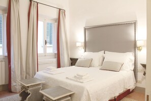 A hotel room with a large bed, two bedside tables, a headboard, and a window with curtains. - Elegant Two-Bedroom Apartment in the Heart of Florence (Firenze)