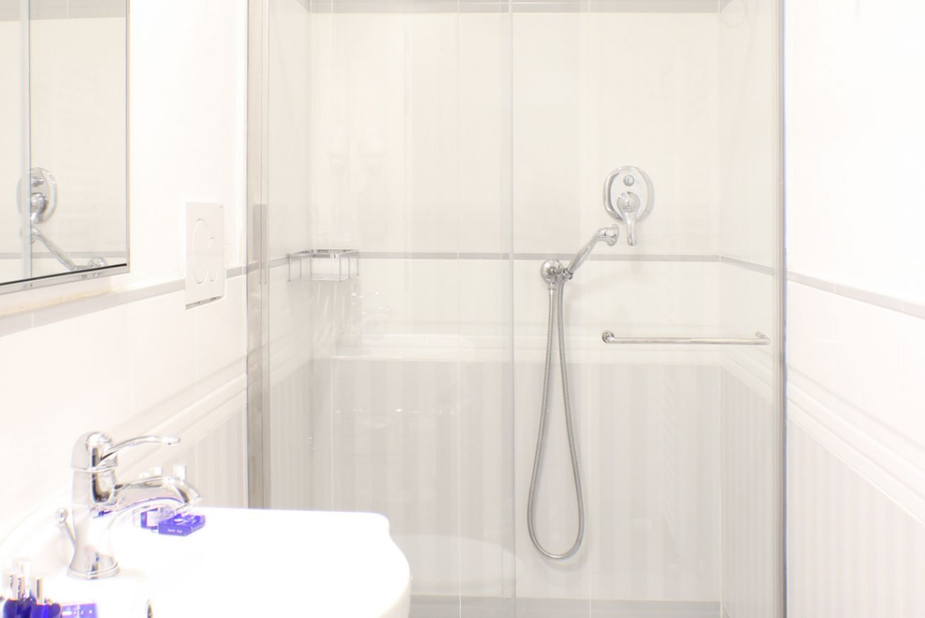 A bathroom with a glass shower enclosure, a white sink, and a mirror.