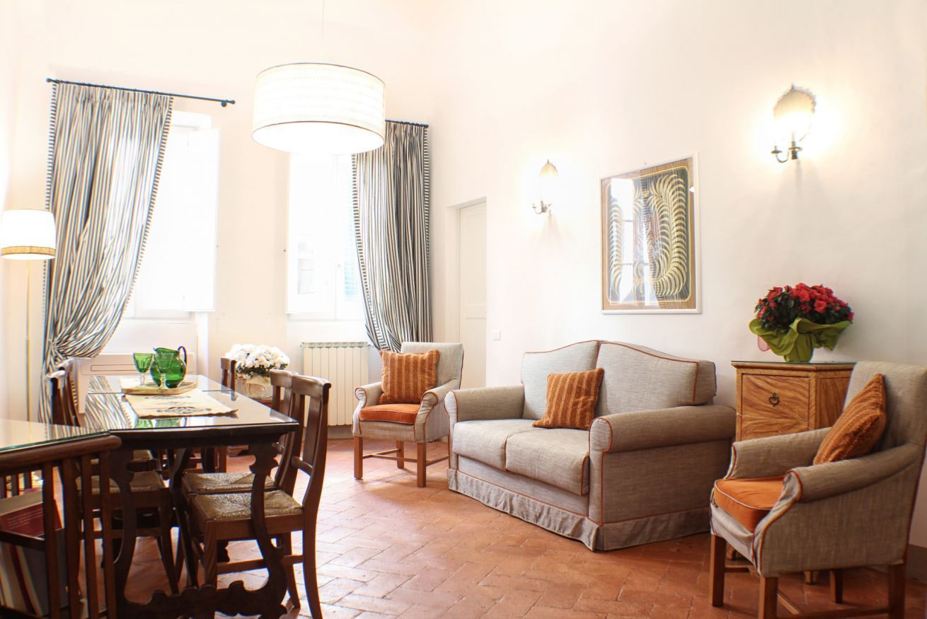 A living room with a glass coffee table, wooden chairs, a sofa, and a side table with a vase of flowers.