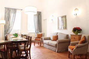 Ein Wohnzimmer mit einem Glastisch, Holzstühlen, einer Couch und einem Beistelltisch mit Blumen.
